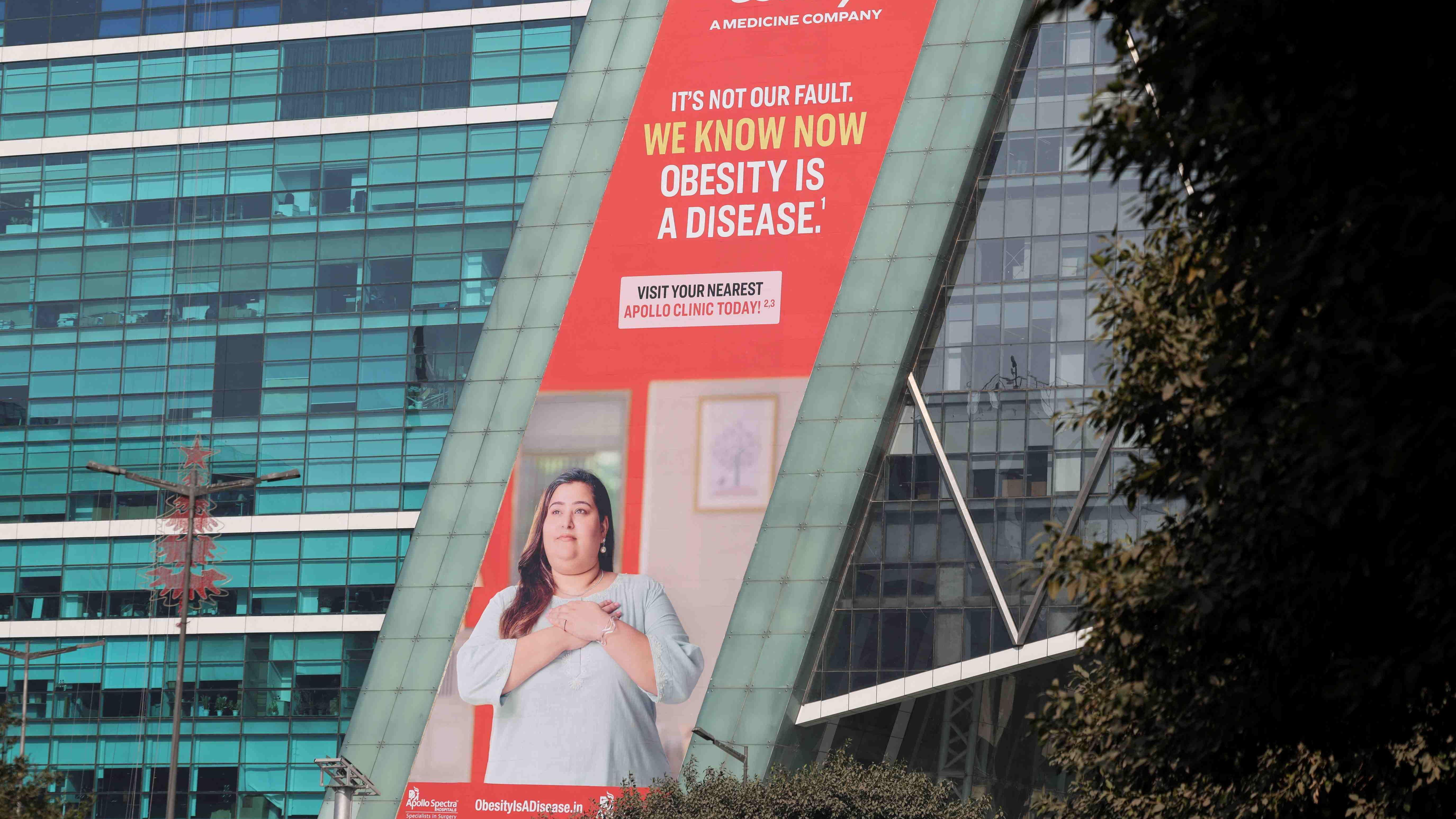 在印度古爾岡的一棟建築上，一塊廣告看板上畫著一位身穿束腰外衣、雙手放在胸前的女性。廣告詞寫道：「這不是我們的錯。我們現在知道肥胖是一種疾病。」
