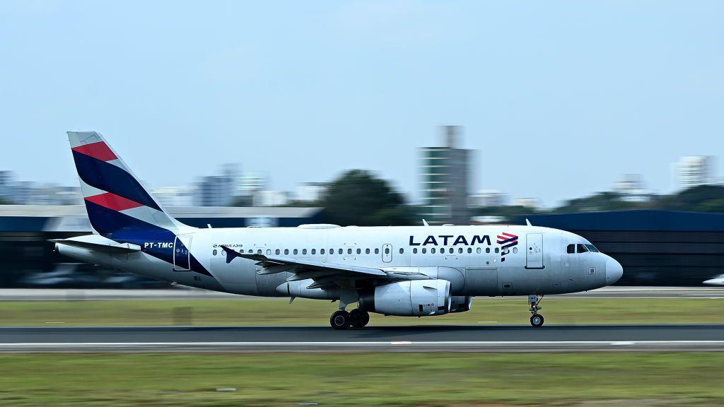 Avião da Latam taxiando na pista do Aeroporto de Congonhas, com a aeronave em movimento e a área urbana ao fundo.