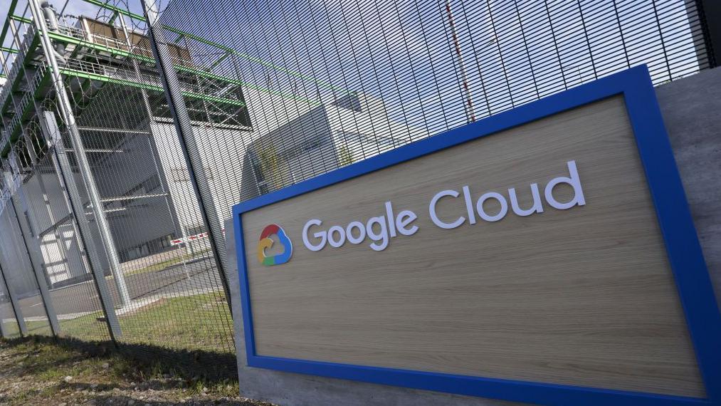 鐵絲網前立著一塊「谷歌雲」（Google Cloud）標誌。後方是一個資料中心。