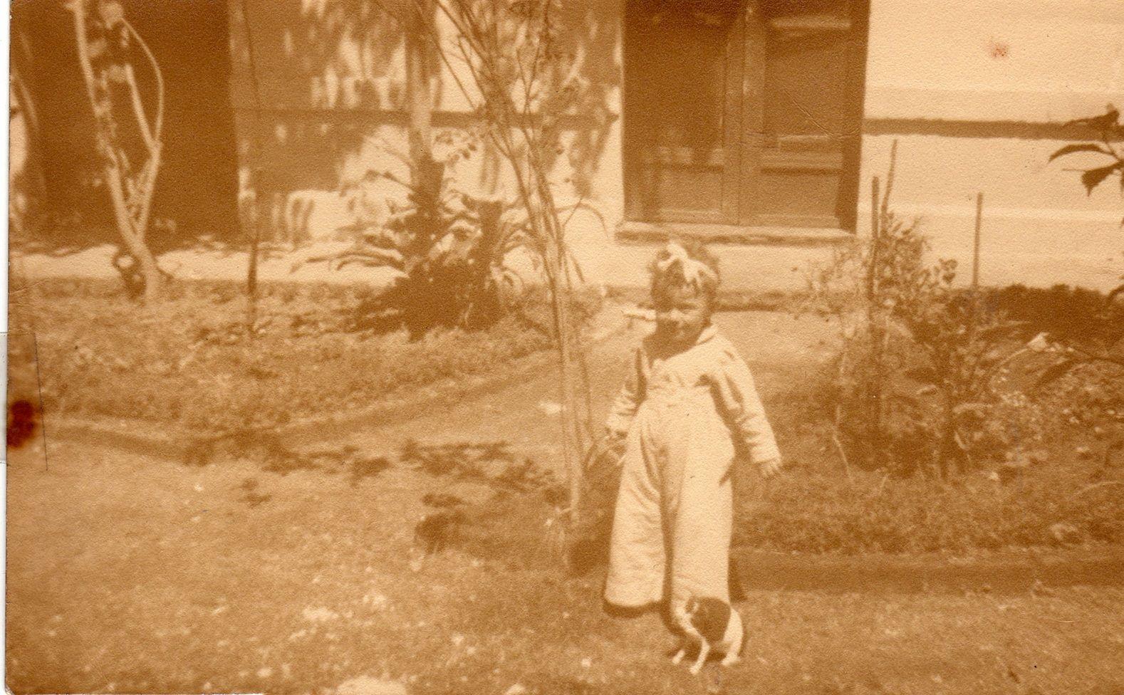 Alejandra Jáidar, con una cinta en la cabeza y vestida con una camisa y un overol blancos, tiene al lado un gato. Está en el jardín de una casa