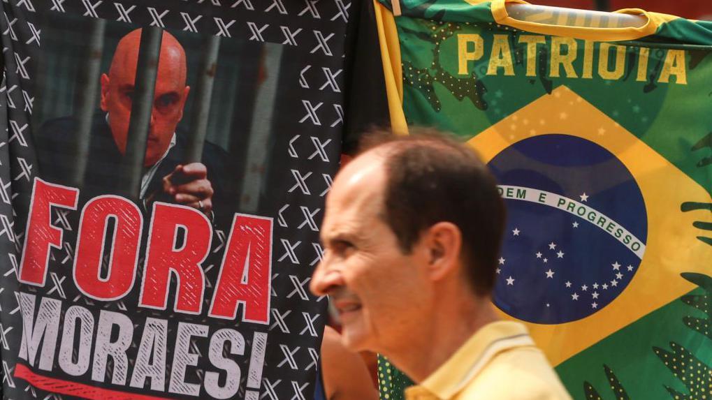 Homem passa em frente a uma bandeira pedindo 