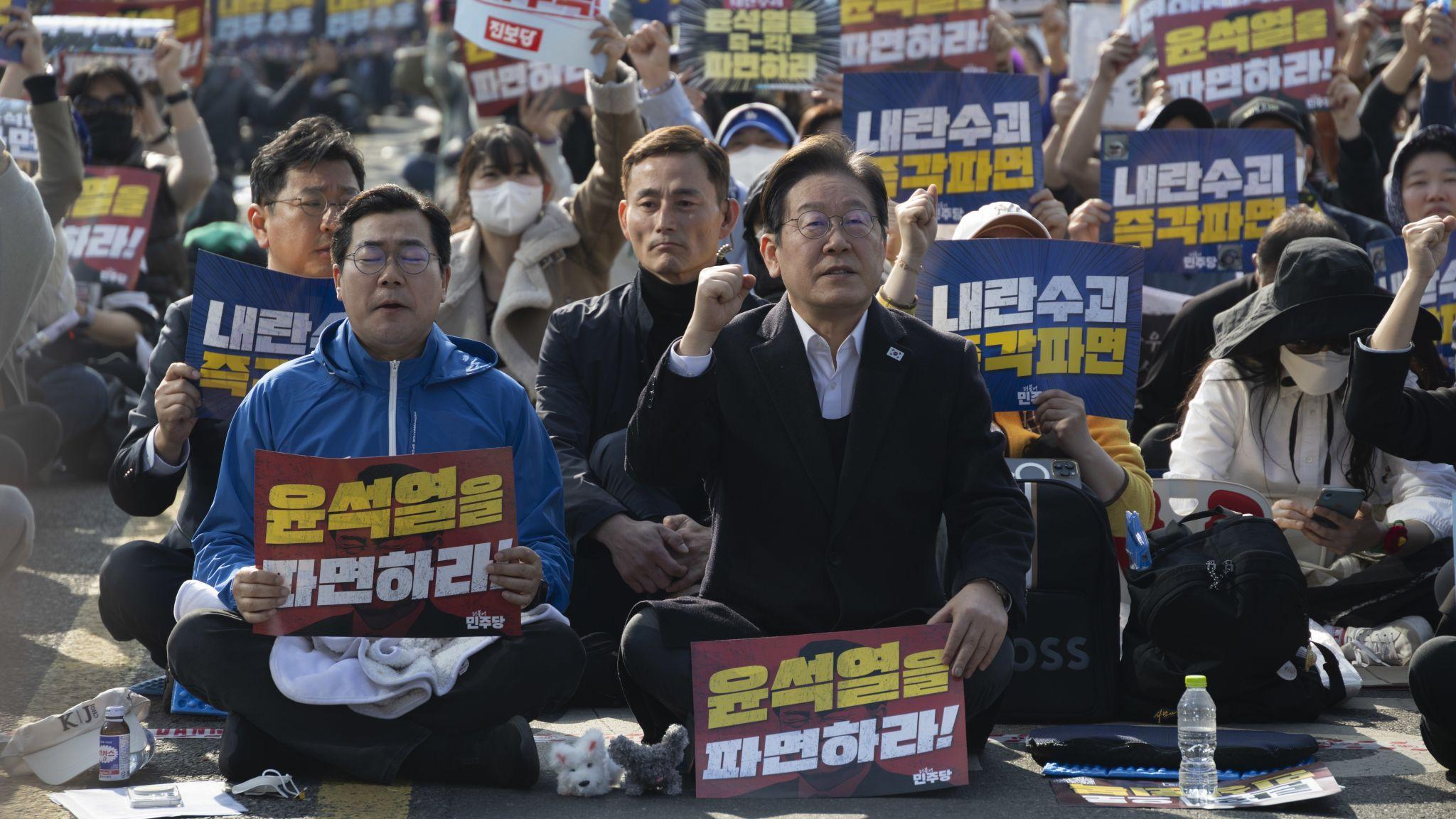 首爾街頭身穿黑色外套的韓國民主黨黨魁李在明(中)拿著反對尹錫悅標語牌帶領支持者叫喊口號(22/3/2025)