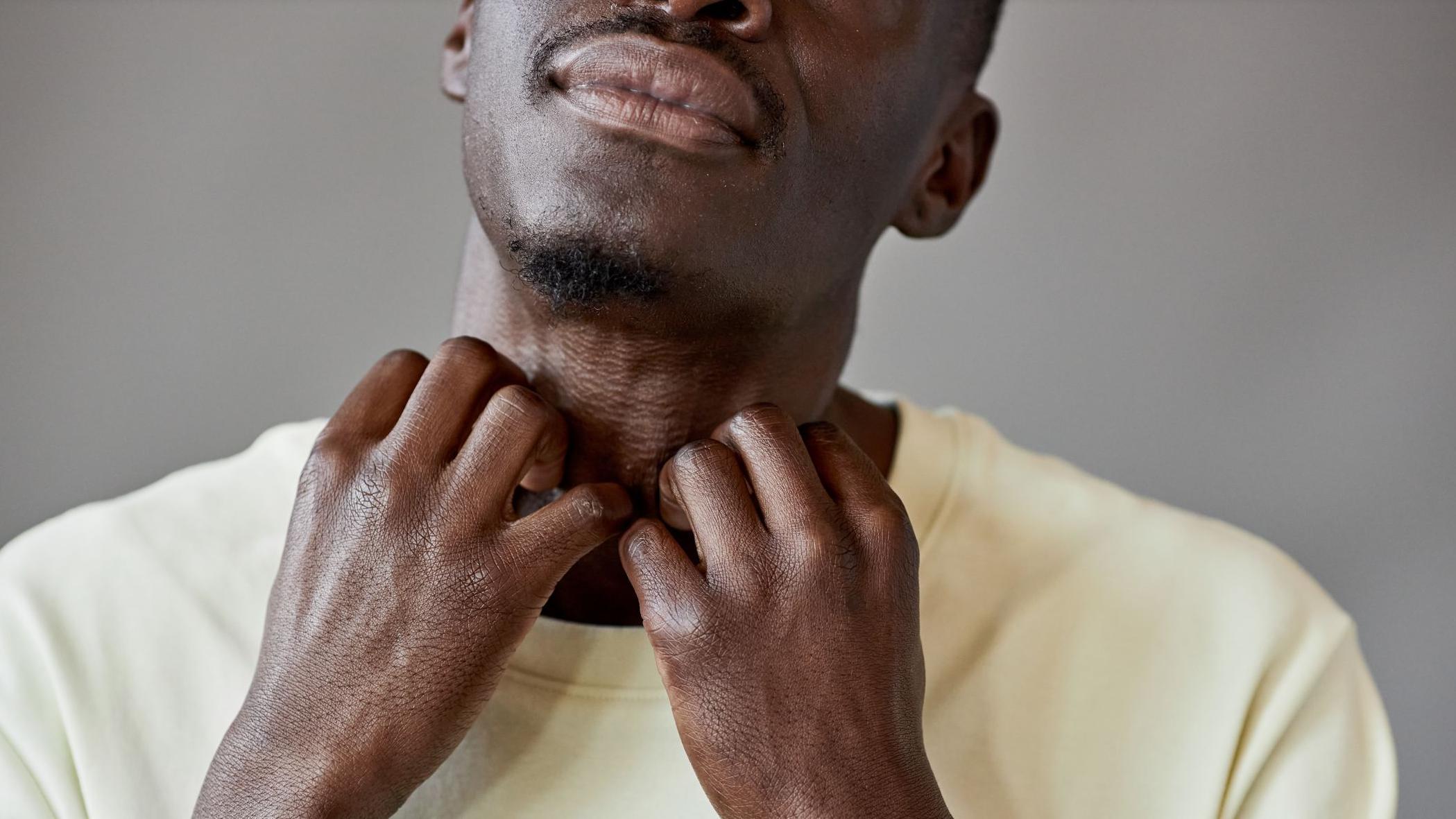 Close de um homem com uma camiseta amarela clara co&ccedil;ando o pesco&ccedil;o com as duas m&atilde;os