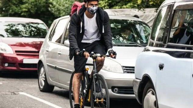 شخص يستقل دراجة هوائية مرتدياً كمامة بين السيارات