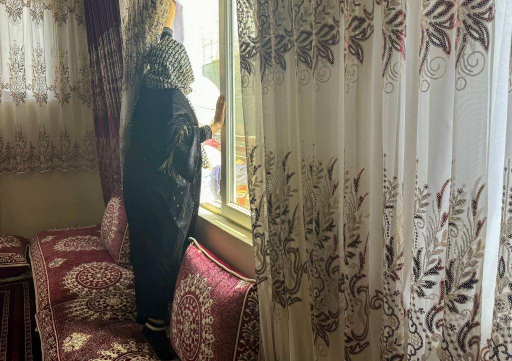 Una mujer afgana cierra las cortinas de su casa