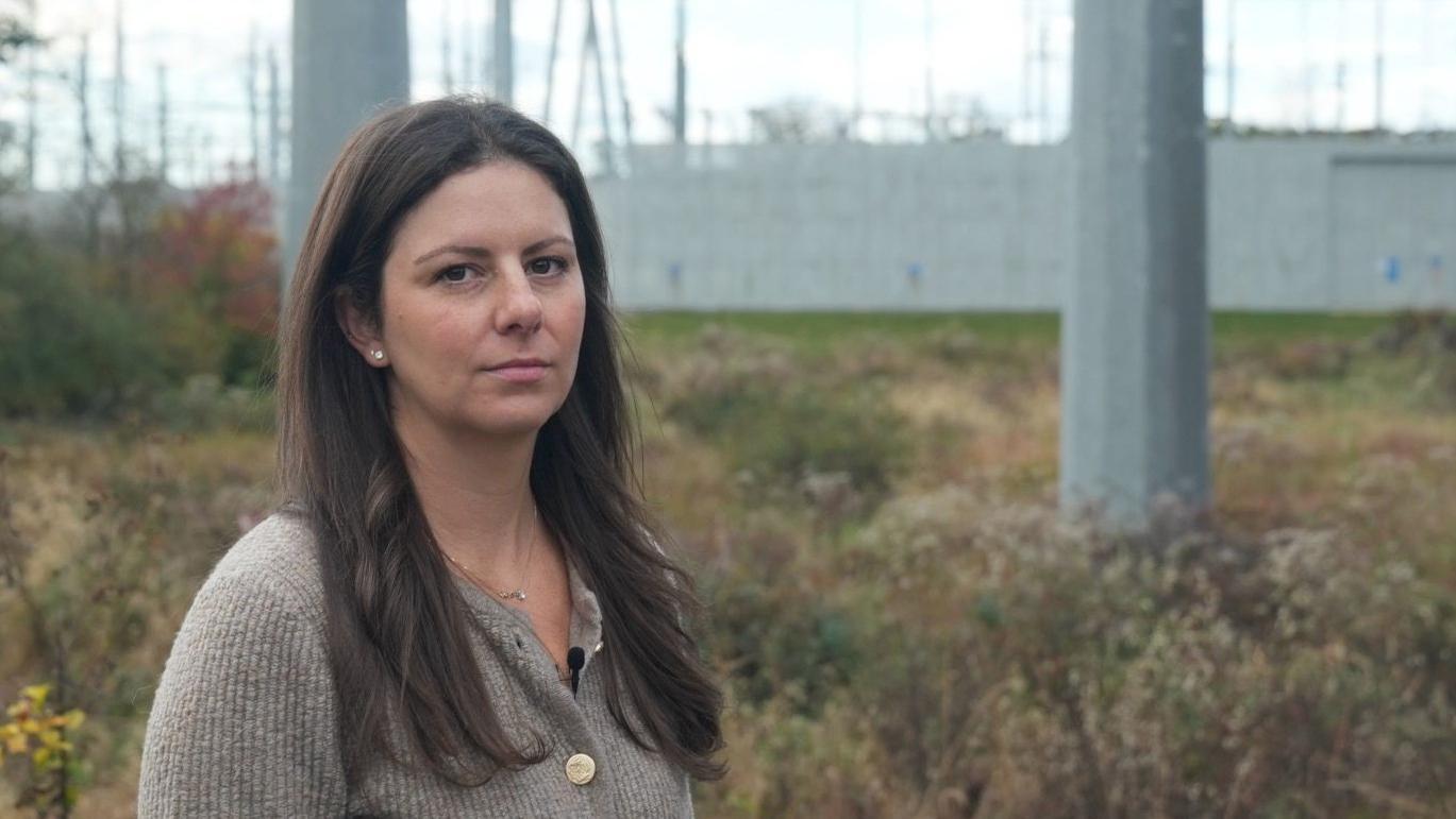 Emily Kasabian se encuentra frente a una subestación con postes gigantes.