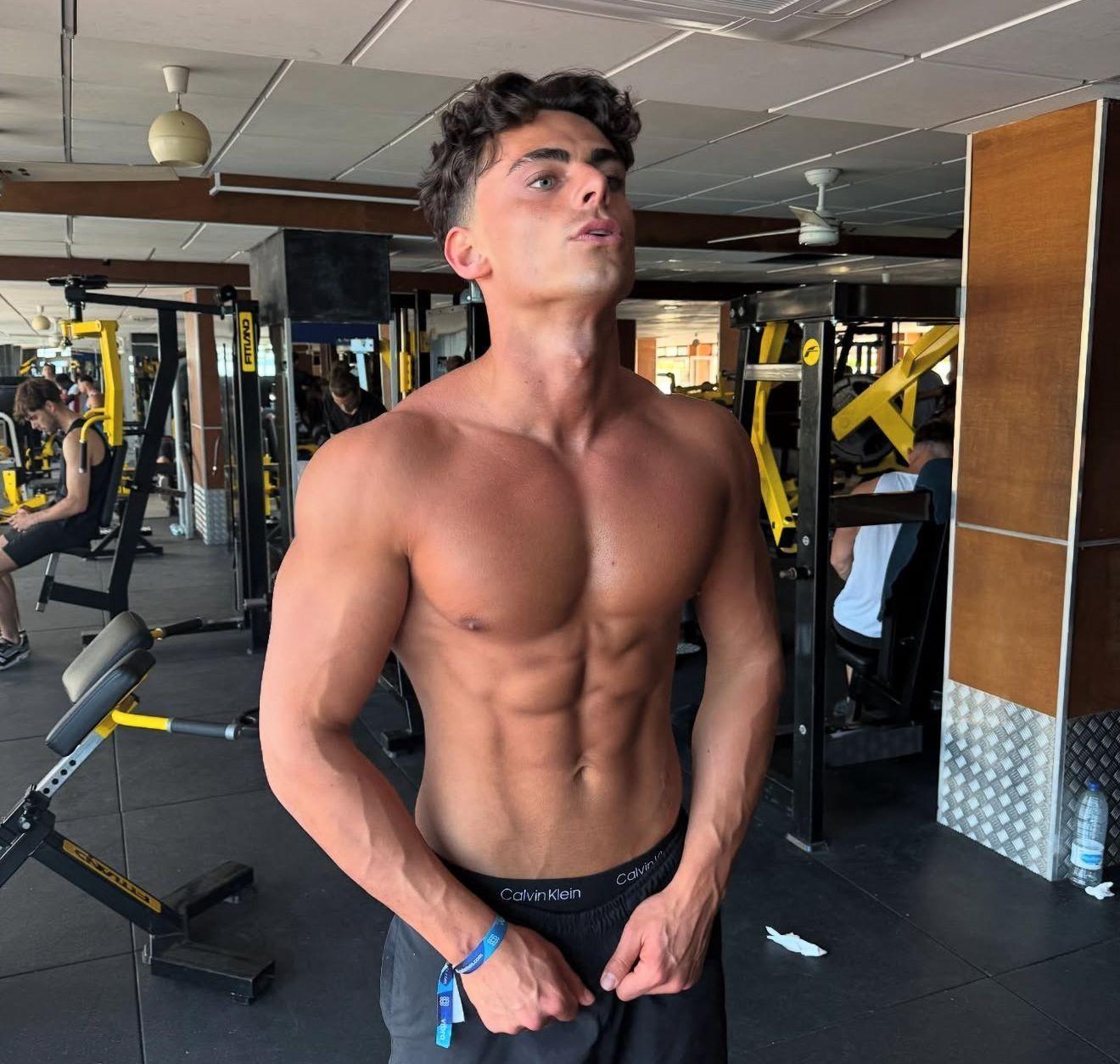 توم في صالة رياضية يرتدي بنطالاً رياضياً دون قميض ويظهر عضلاته.