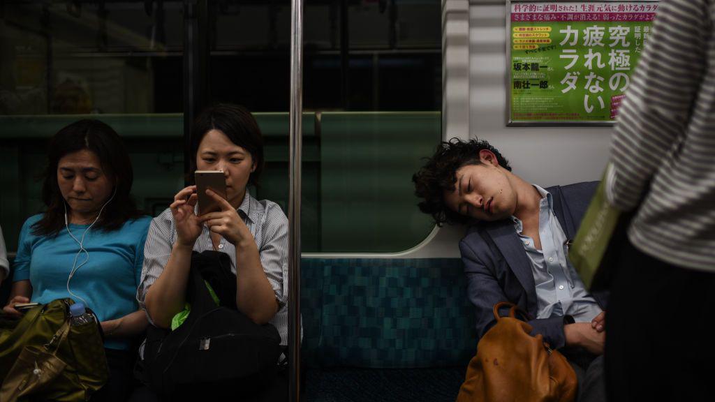 Tr&ecirc;s pessoas em um vag&atilde;o de metr&ocirc;. O homem &agrave; direita est&aacute; dormindo