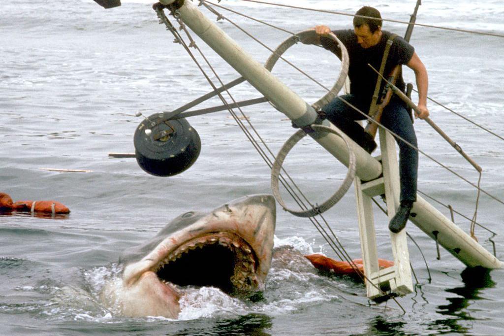 No set de gravação de 'Tubarão', o ator Roy Scheider (1932-2008) aparece sobre os restos de um barco que afunda, enquanto o tubarão o espera com a boca aberta na água