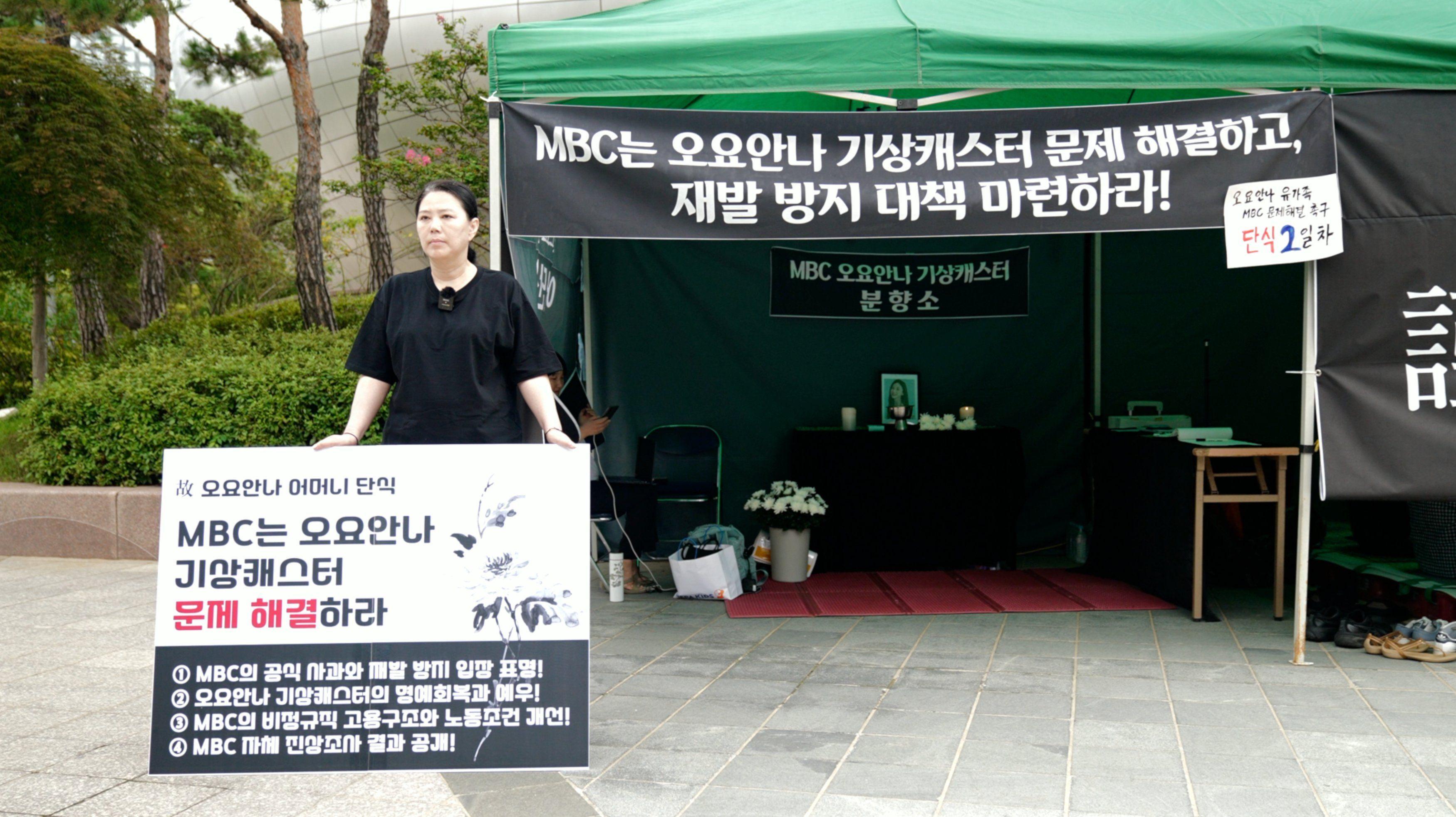 오요안나 기상캐스터의 어머니 장연미 씨가 'MBC는 오요안나 기상캐스터 문제 해결하라'는 팻말을 들고 MBC 앞에서 단식 농성을 하고 있다. 그의 뒤에는 분향소가 차려져 있다.