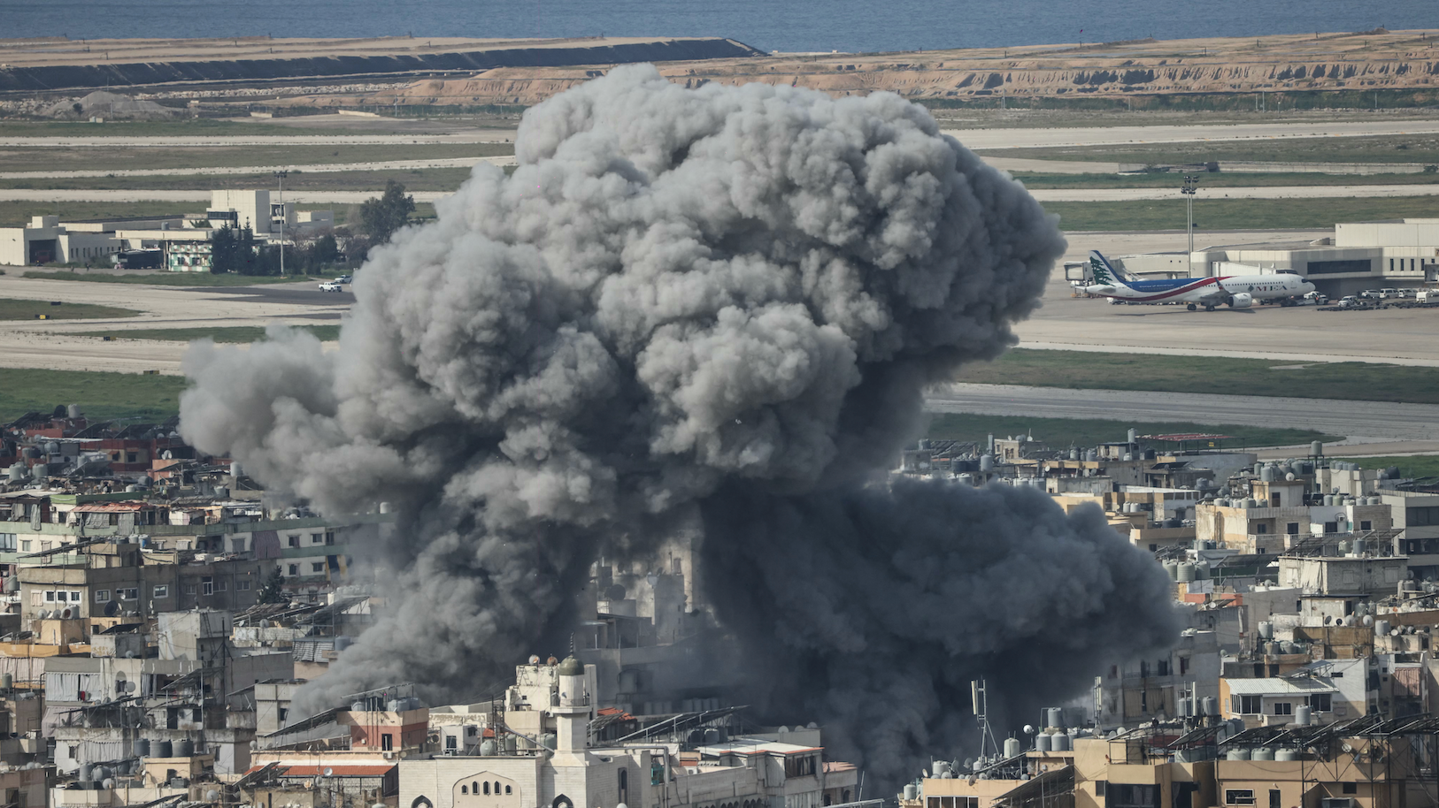 Coluna de fuma&ccedil;a subindo do local de um ataque a&eacute;reo israelense dirigido ao bairro de Al Lailaki, no sul de Beirute, com o aeroporto internacional da cidade vis&iacute;vel ao fundo, no dia 4 de mar&ccedil;o de 2026