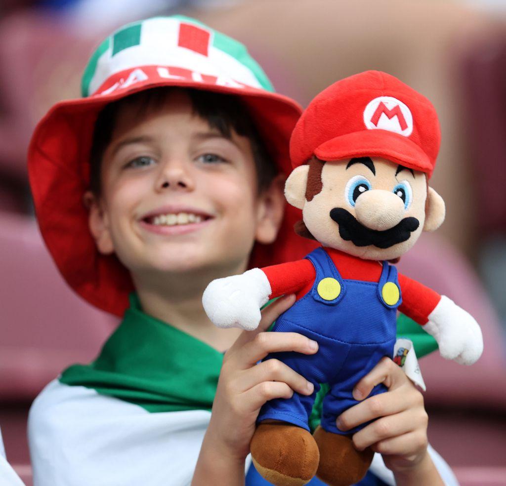 Un joven aficionado de la selección italiana posa para una foto mientras sostiene un muñeco de peluche de Super Mario, disfrutando del ambiente previo al partido de cuartos de final de la Eurocopa Femenina de la UEFA 2025 entre Noruega e Italia, que se disputará el 16 de julio de 2025 en el Estadio de Ginebra, en Ginebra, Suiza.