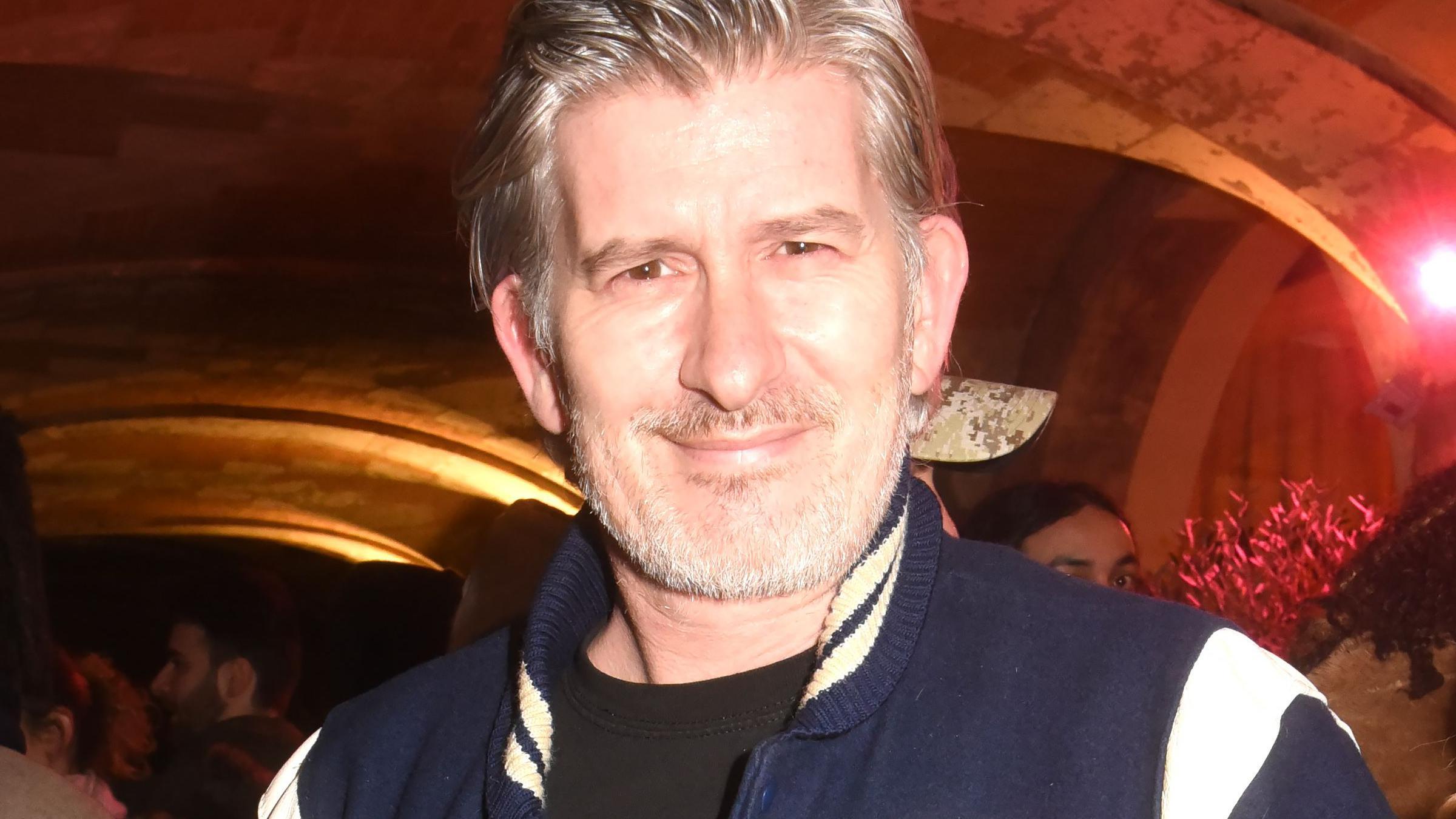 El músico y DJ Kavinsky sonriendo y vistiendo una chaqueta azul en el desfile de moda Otoño/Invierno 2021 de Gaëlle Constantini en París, 2020.