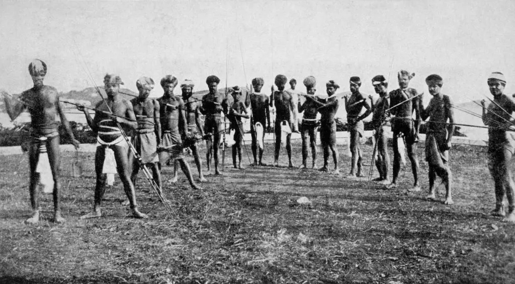 مجموعة من جنود الكاناك في زي الحرب، عراة الصدور يمسكون بأسلحة بدائية ويرتدون قبعات، عام 1906