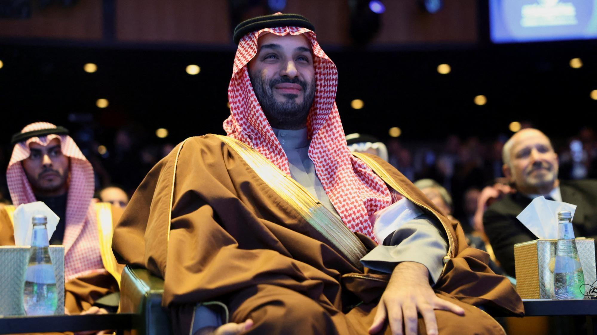 ولي العهد السعودي الأمير محمد بن سلمان يحضر منتدى الاستثمار الأمريكي السعودي بواشنطن في 19 نوفمبر/تشرين الأول 2025، ويجلس مُبتسماً، مرتدياً عُقالاً وجلباباً وعباءة.