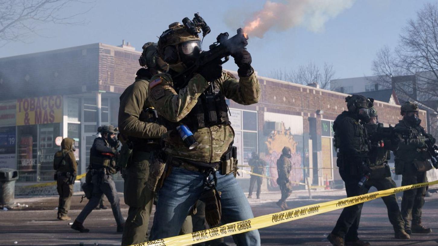 Un grupo de agentes con cascos, mascaras antigás y chalecos disparan lo que parecen ser bombas de gas en Mineápolis. 