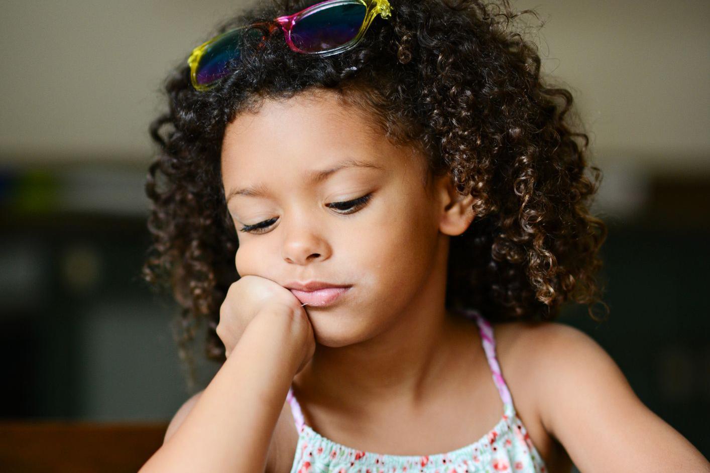 Una niña con la mirada perdida mientras apoya su cara sobre su brazo