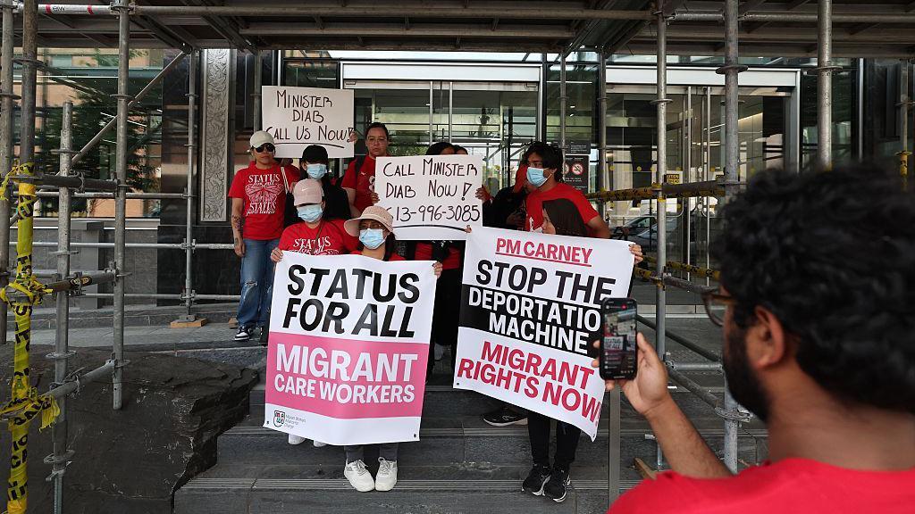 Trabalhadoras domésticas migrantes ocupam o saguão do prédio federal de imigração canadense no Dia Internacional das Trabalhadoras Domésticas (16 de junho). As trabalhadoras, vestidas de vermelho e segurando cartazes, exigem uma reunião com a ministra da Imigração, Lena Diab, em Toronto