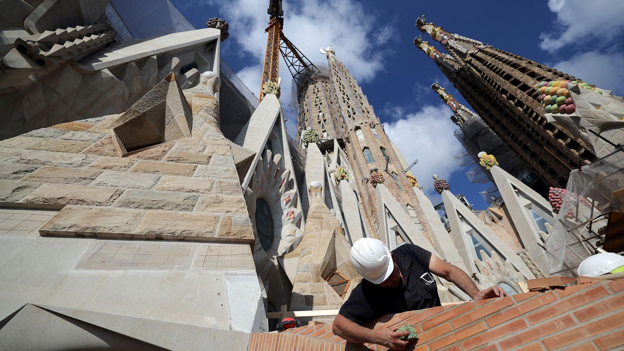 Un obrero con casco blanco y camiseta negra en trabajos de construcción con varias torres elevándose a sus espaldas.

