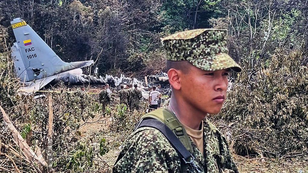 Un soldado joven, con gesto serio, en el lugar donde cayó el Hércules C-130 de la Fuerza Aérea de Colombia. En el fondo se ven restos de la aeronave.