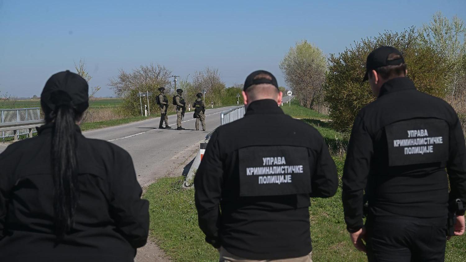 Tri policajca stoje leđima okrenuta kameri ispred njih trojica vojnih policajaca pod punom opremom na cesti