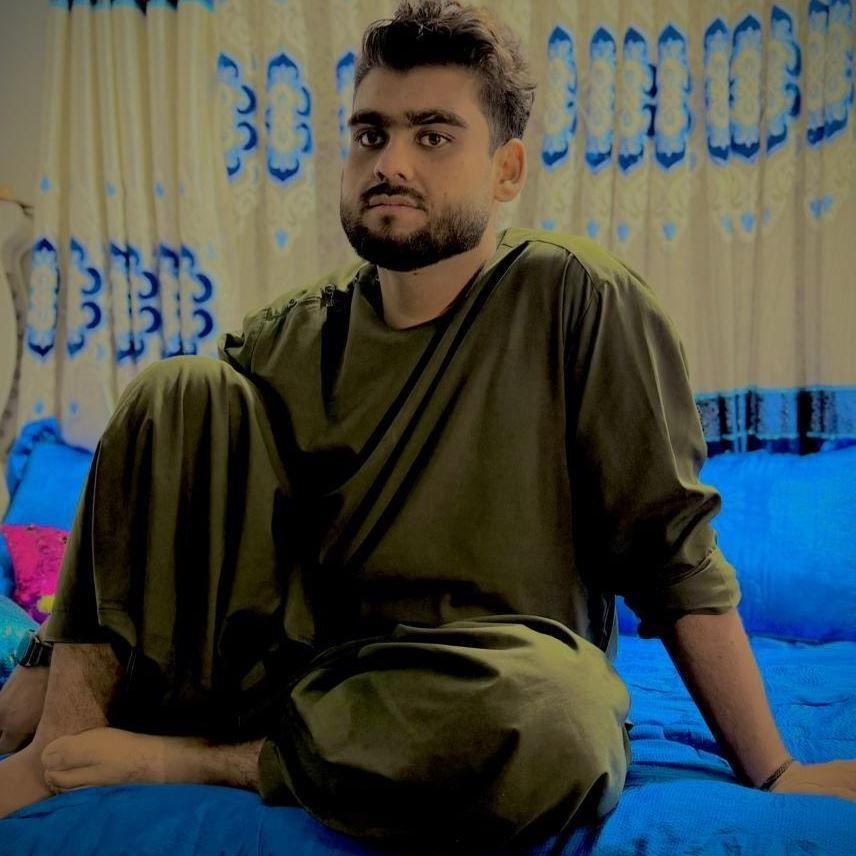 Qudratullah sitting on a blue bedsheet