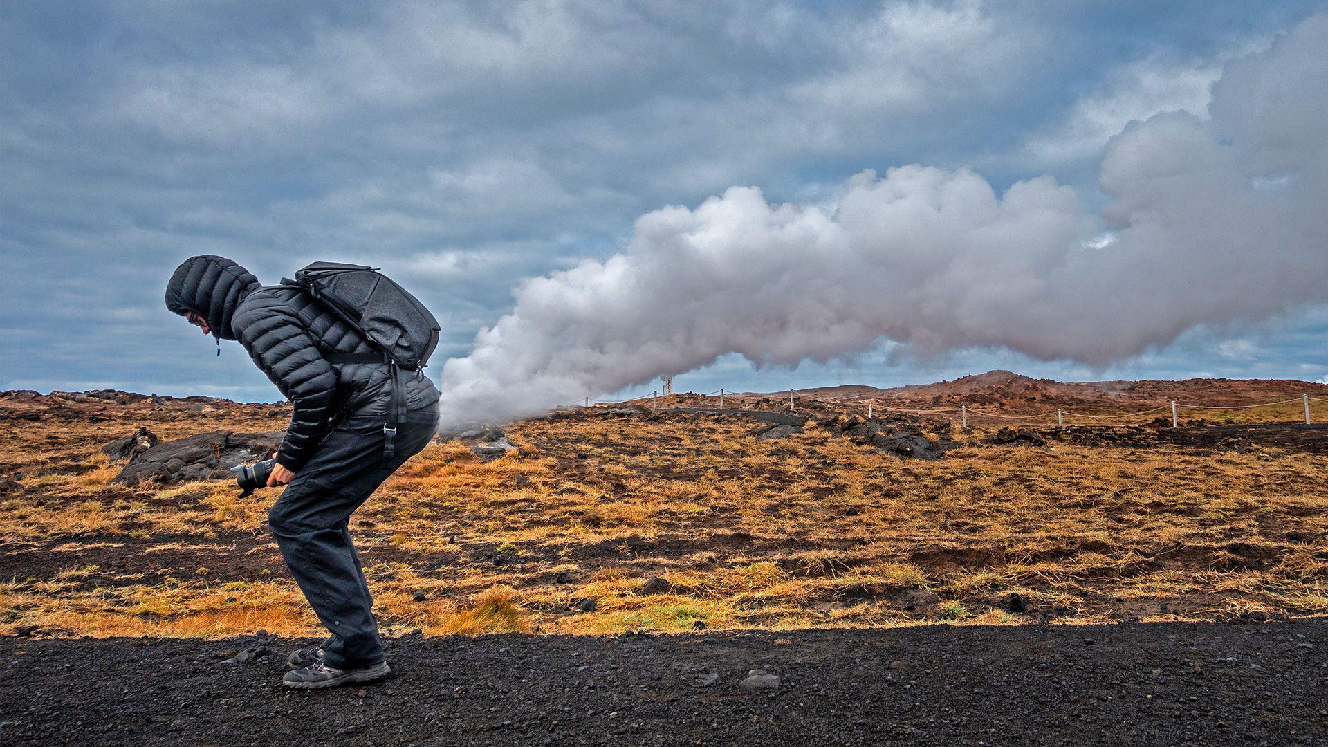 Fotografija prikazuje čoveka u kratkoj perjanoj jakni sa kapuljačom na glavi, u pantalonama i cipelama za planinarenje. Postavio se tako da izgleda kao da mu oblaci izlaze iz zadnjice 
