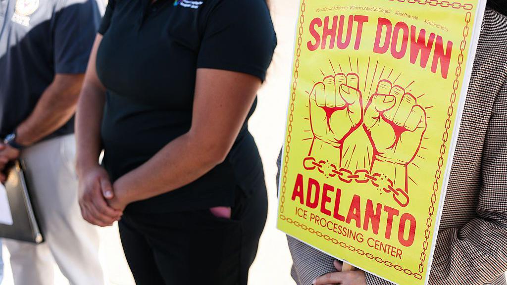 Una persona sostiene un cartel que dice "Cierre Adelanto" después de que a los congresistas demócratas por California Raul Ruiz y Norma Torres se les negara la entrada para una visita de supervisión del Congreso al centro de detención del Centro de Procesamiento de ICE de GEO Group en Adelanto, California, el 11 de julio de 2025. (Foto de Patrick T. Fallon / AFP) (Foto de PATRICK T. FALLON/AFP vía Getty Images)