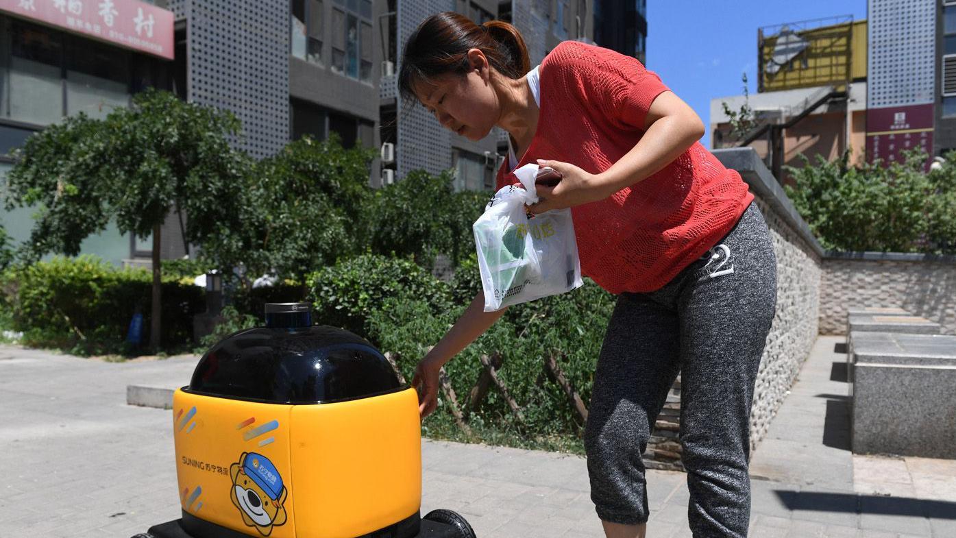 Uma mulher recolhe compras entregues por um rob&ocirc; da Zhen Robotics em um condom&iacute;nio residencial
