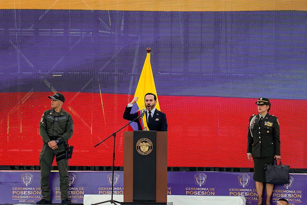 De la Espriella da su discurso de posesión sobre un escenario frente a una pantalla que muestra la bandera de Colombia y acompañado de dos representantes de la fuerza pública, un hombre y una mujer.