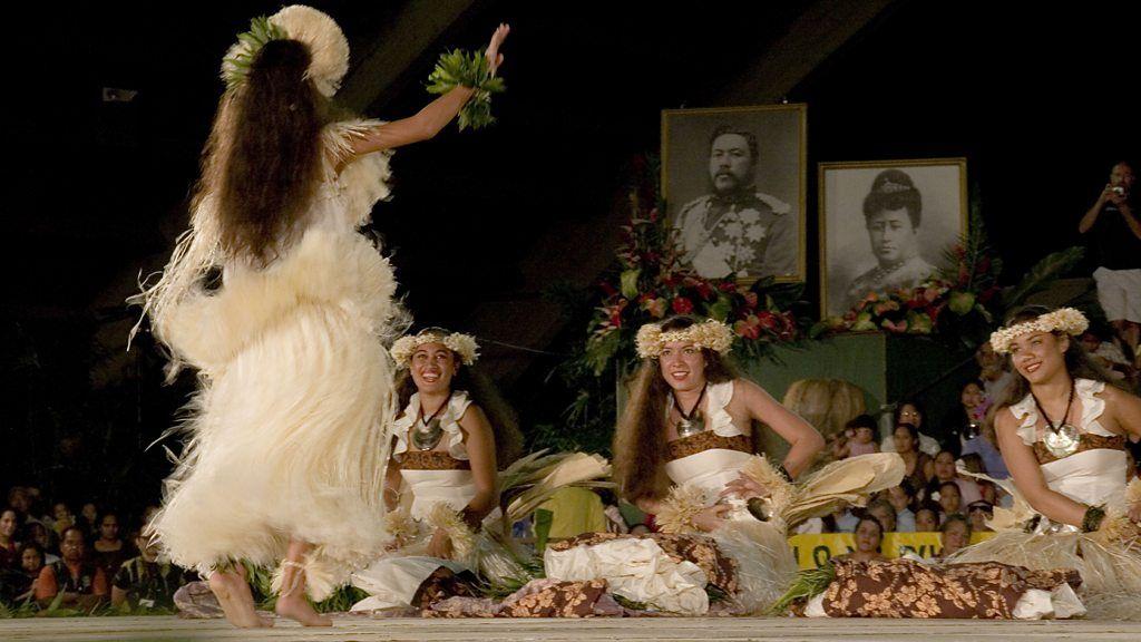 Dançarinas de hula se apresentam ao público frente a dois retratos reais