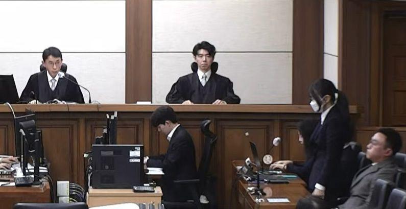 법정 내부에서 재판부와 방청석 앞에 앉은 관계자들이 보이고, 마스크를 쓴 김건희 여사가 1심 선고를 받는 모습이 보인다. 