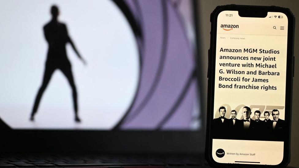 Imagem dos créditos iniciais de James Bond com um celular na frente anunciando que a Amazon está assumindo a franquia.