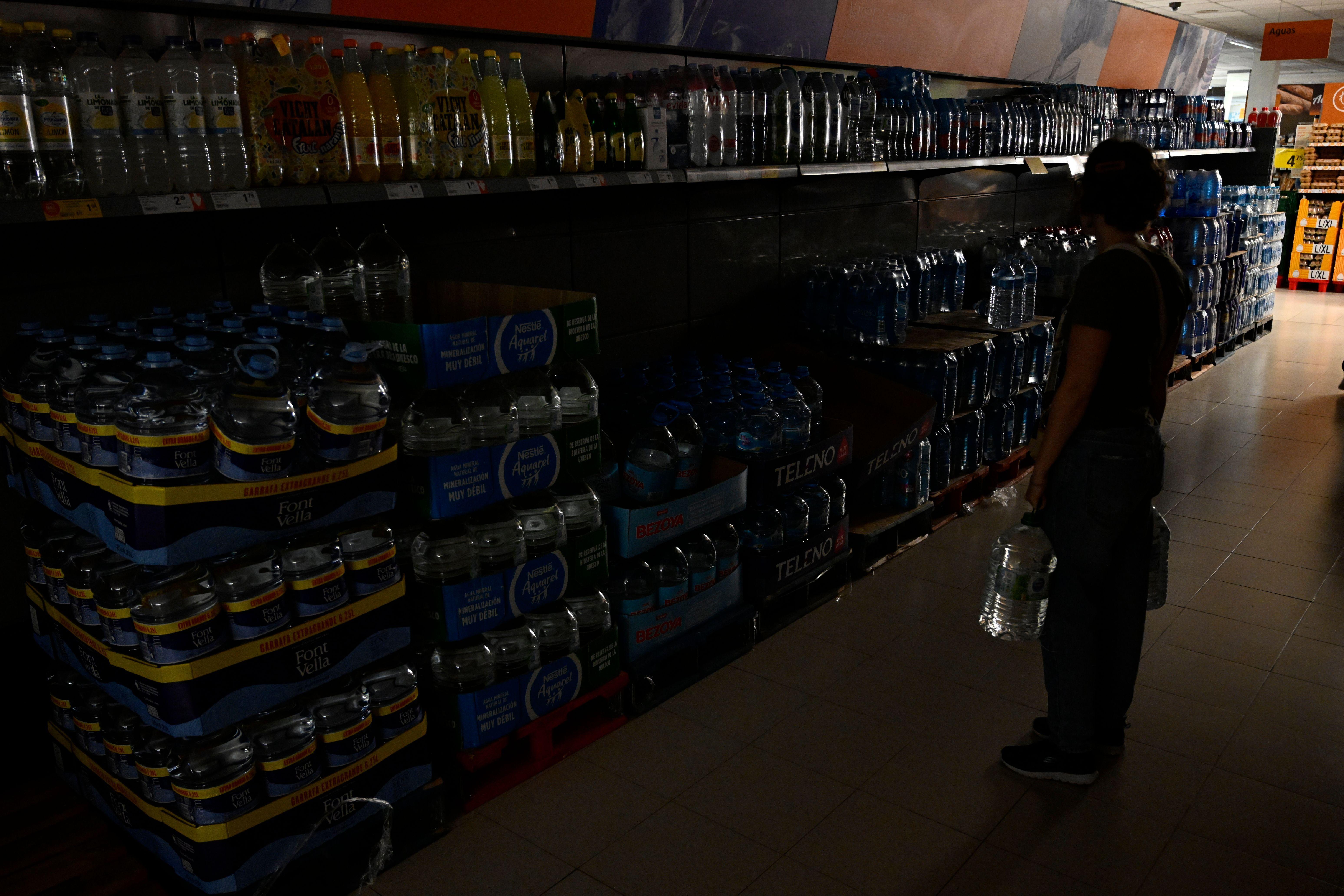 Mulher segura recipientes de água em um supermercado sem luz, em Castellón, na Espanha