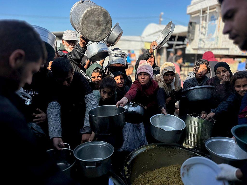 يمدّ فلسطينيون أواني معدنية وحاويات أخرى باتجاه متطوعين خلال عملية توزيع غذائي في خان يونس بقطاع غزة، في 23 ديسمبر/كانون الأول 2025. 