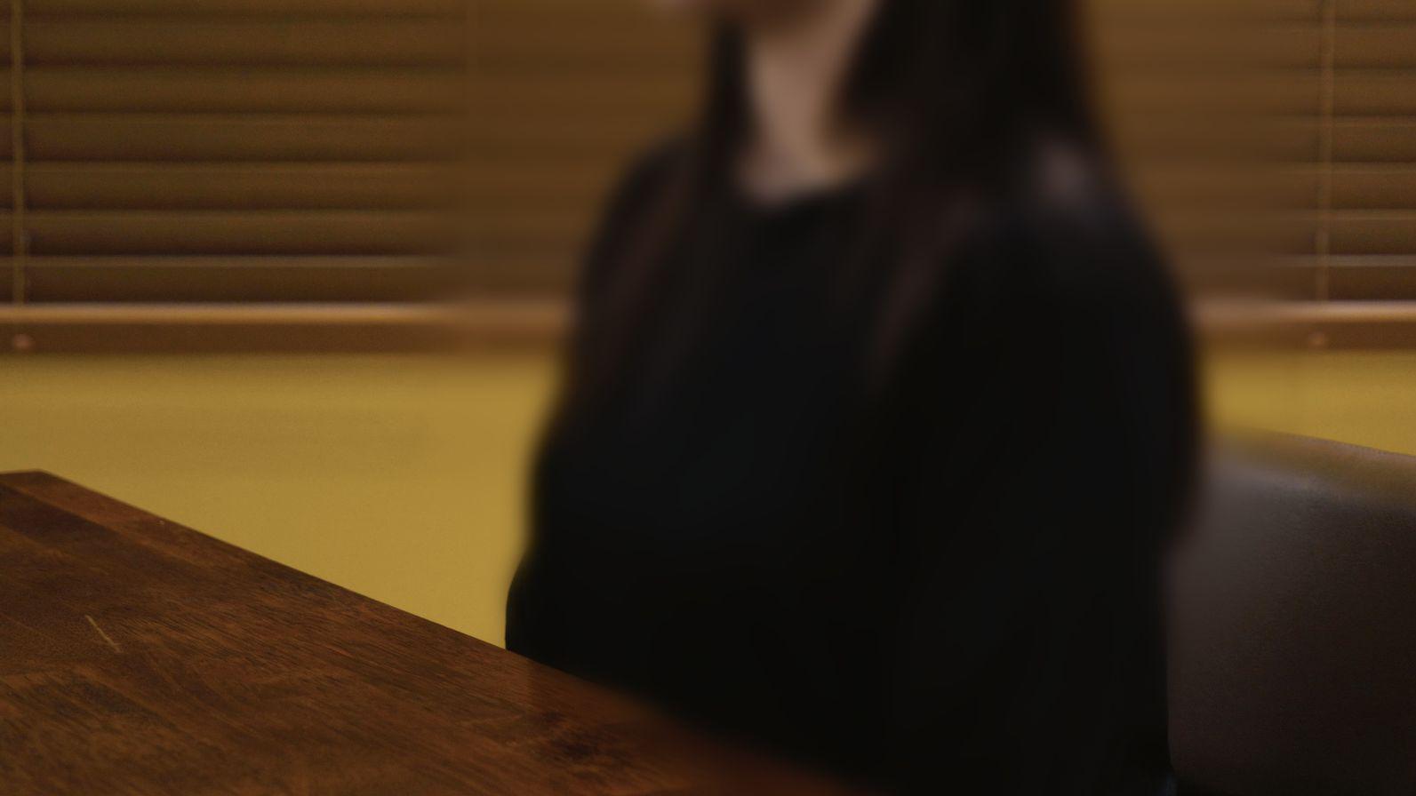 Una imagen borrosa de una mujer con una blusa negra, sentada detrás de un escritorio.