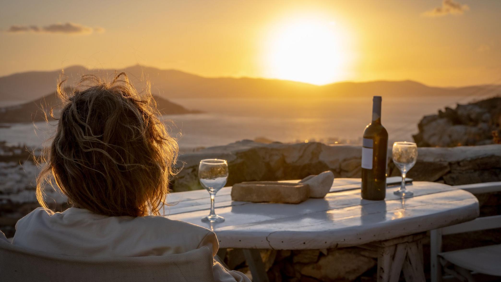 Mujer bebiendo una copa de vino y admirando un atardecer en el mar