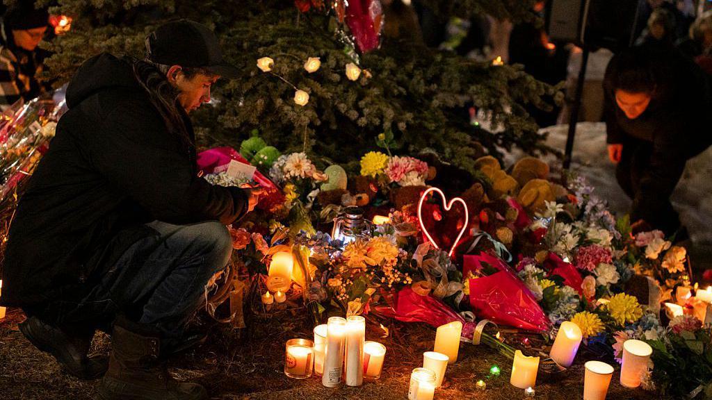 Un miembro de la comunidad coloca flores en un monumento conmemorativo durante una vigilia con velas por las víctimas de la escuela secundaria Tumbler Ridge, donde tuvo lugar un tiroteo masivo un día antes, en la pequeña ciudad de Tumbler Ridge, Columbia Británica.