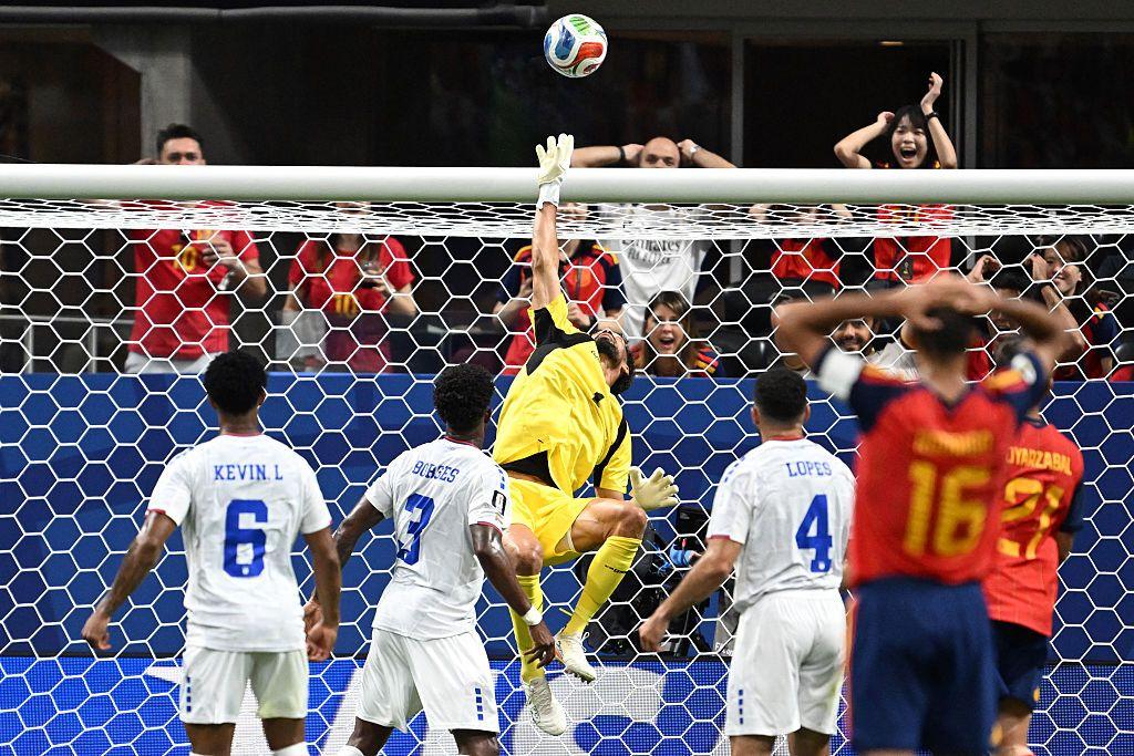Vozinha alza la mano para detener un balón enviado por jugador vestido con la camiseta de España. 