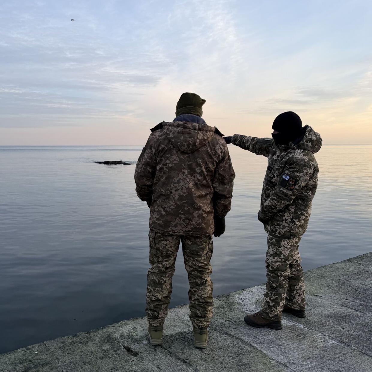 Dos soldados de la marina de Ucrania miran desde un muelle hacia el mar Negro.