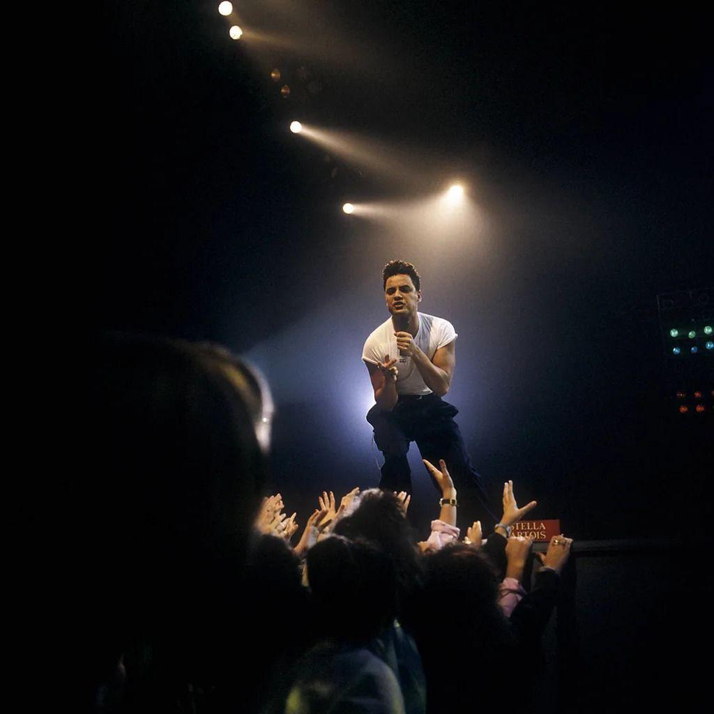 환호하며 손을 뻗는 관중들 사이로 보이는 무대 위 닉 케이먼