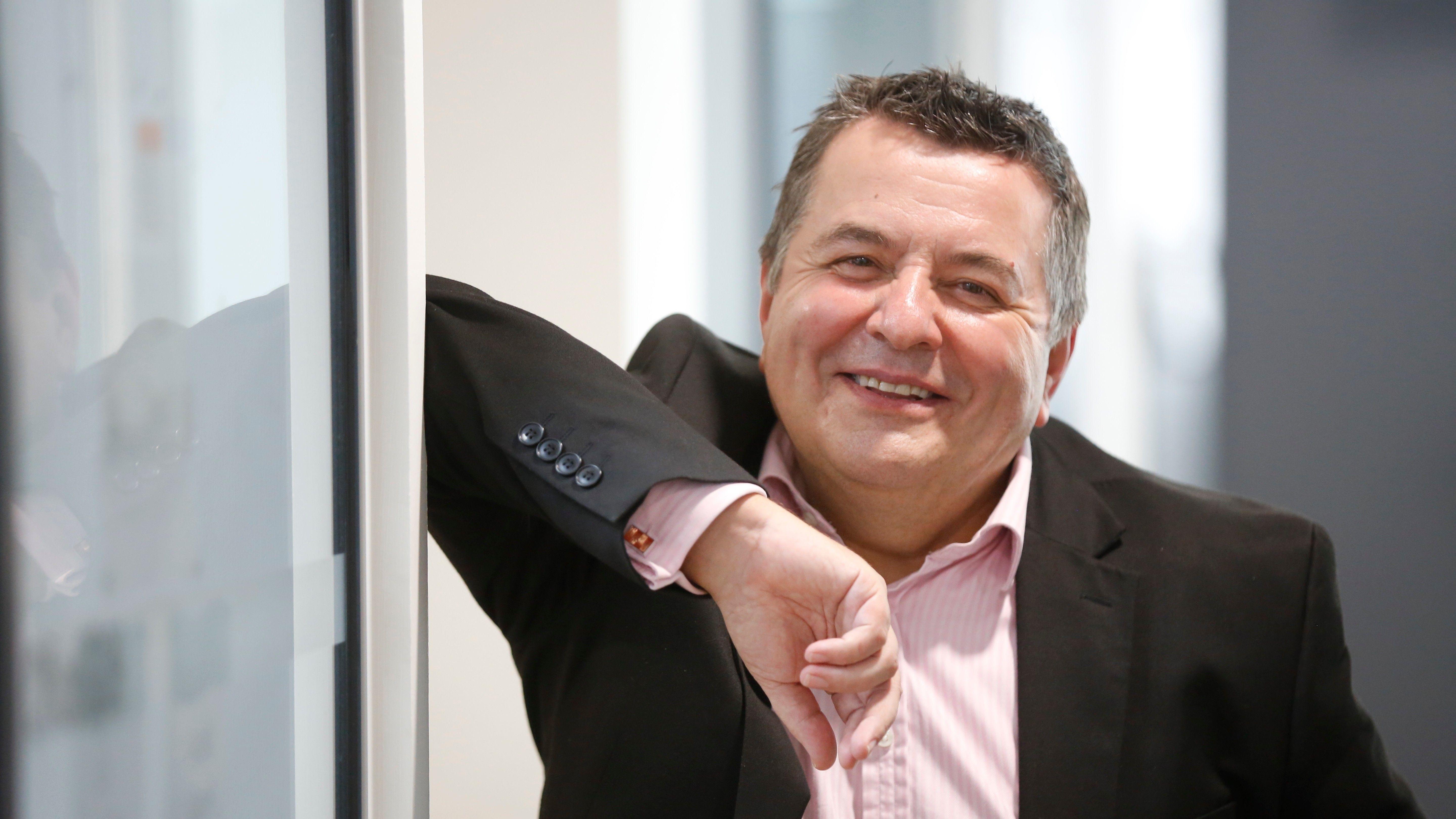 리처드 스켈렛이 검은색 재킷과 분홍색 셔츠를 입고 카메라를 바라보며 미소 짓고 있다