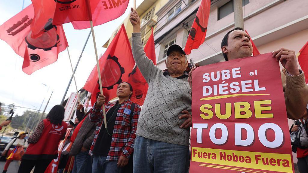 Manifestantes gritan consignas mientras sostienen un cartel que dice: "Sube el diésel, sube todo. Fuera Noboa Fuera". Como parte del paro nacional del 2 de octubre de 2025 en Quito, Ecuador.
