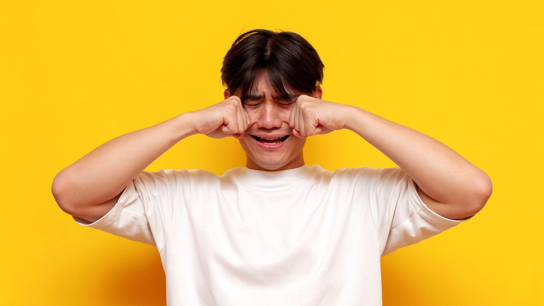 رجل يفرك عينيه وهو يبكي بشكل درامي، على خلفية صفراء زاهية