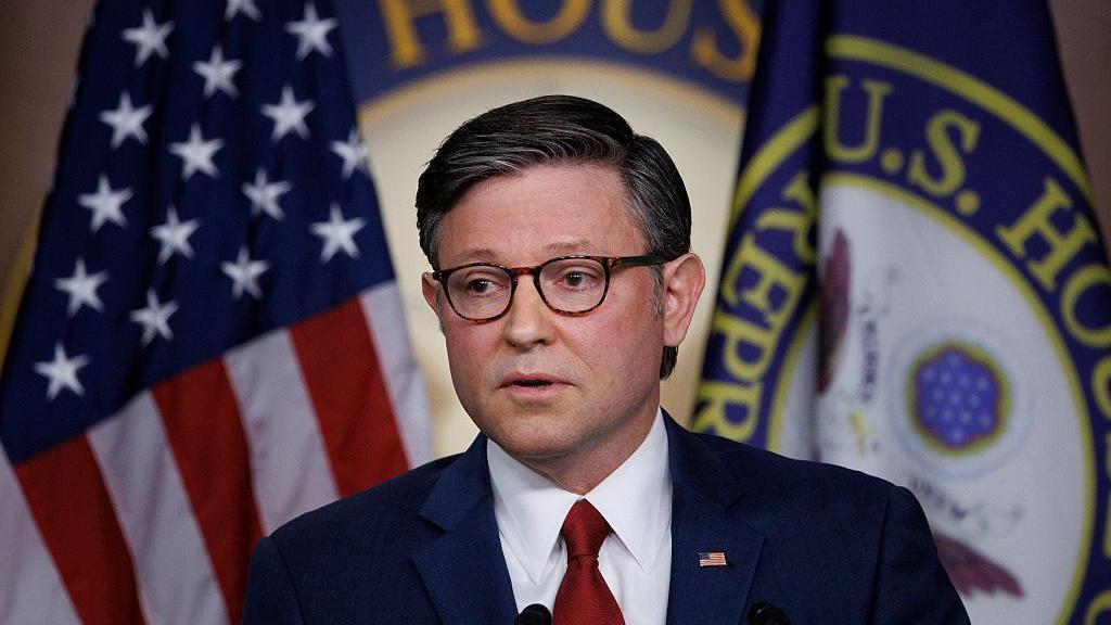 El presidente de la Cámara de Representantes de EE. UU., Mike Johnson (republicano por Luisiana), durante una conferencia de prensa en el Capitolio. Detrás tiene las banderas de Estados Unidos y de la Cámara de Representantes.