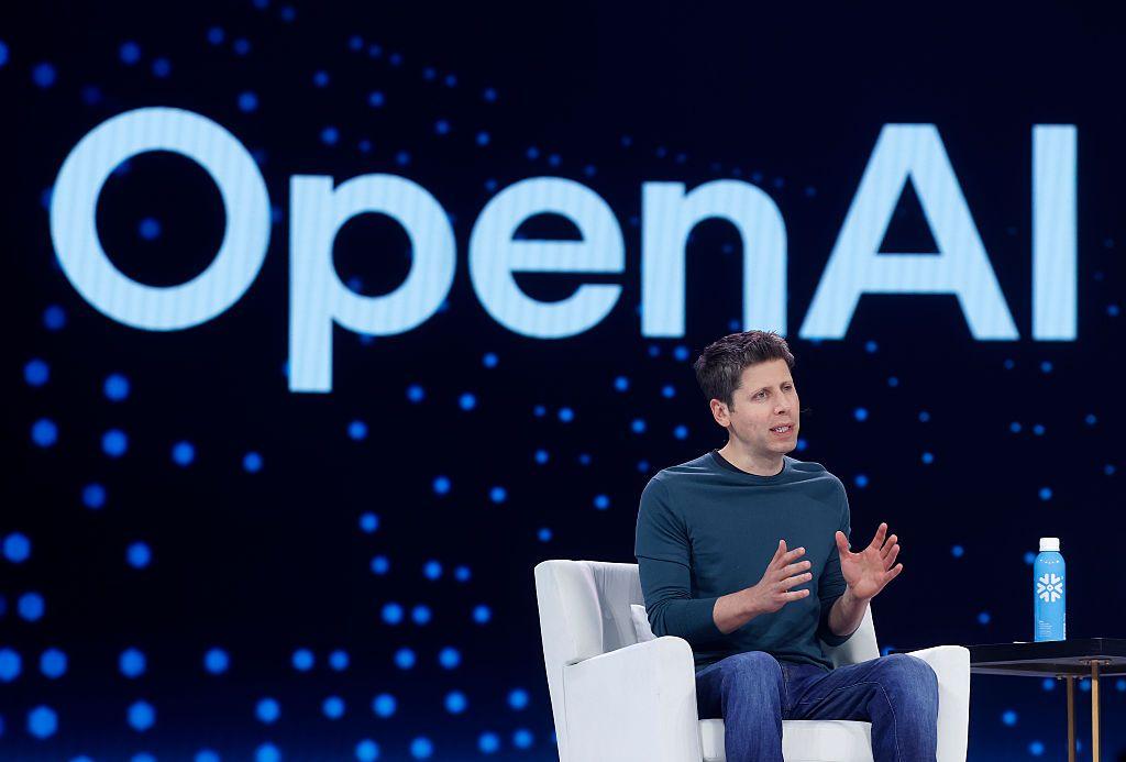 Sam Altman, CEO da OpenAI, sentado em sofá branco falando ao público em evento corporativo