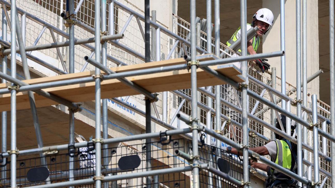 Građevinska skela i dva radnika u prslucima i sa kacigama na glavi