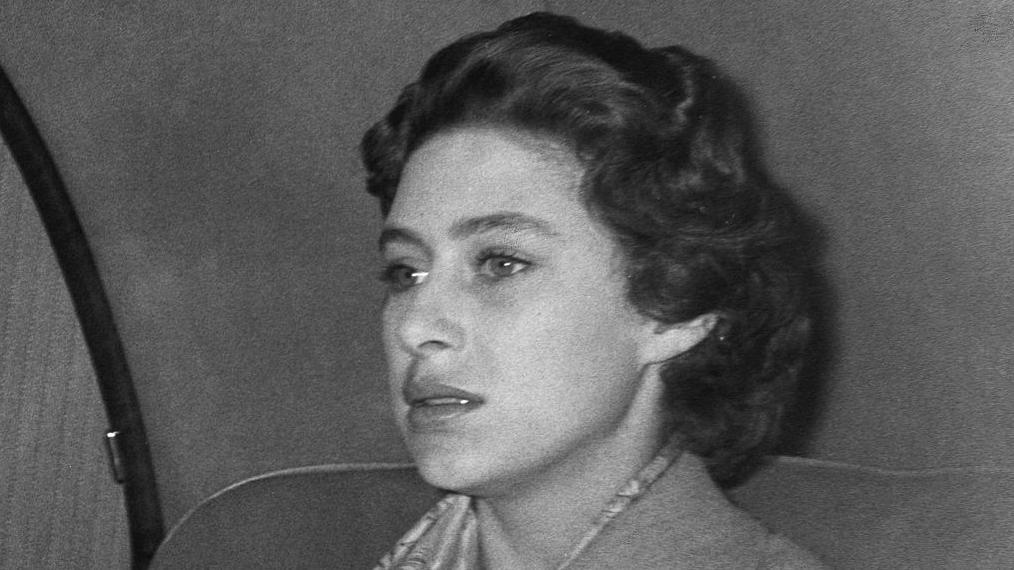 Imagen cerrada de una mujer con pelo  corto negro dentro de un automóvil con expresión de angustia.