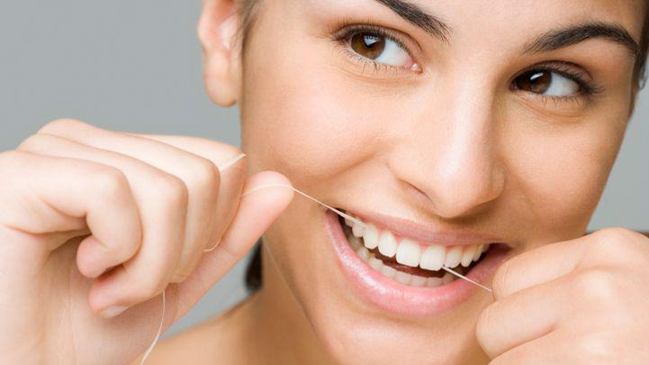 A woman smiles while using dental floss