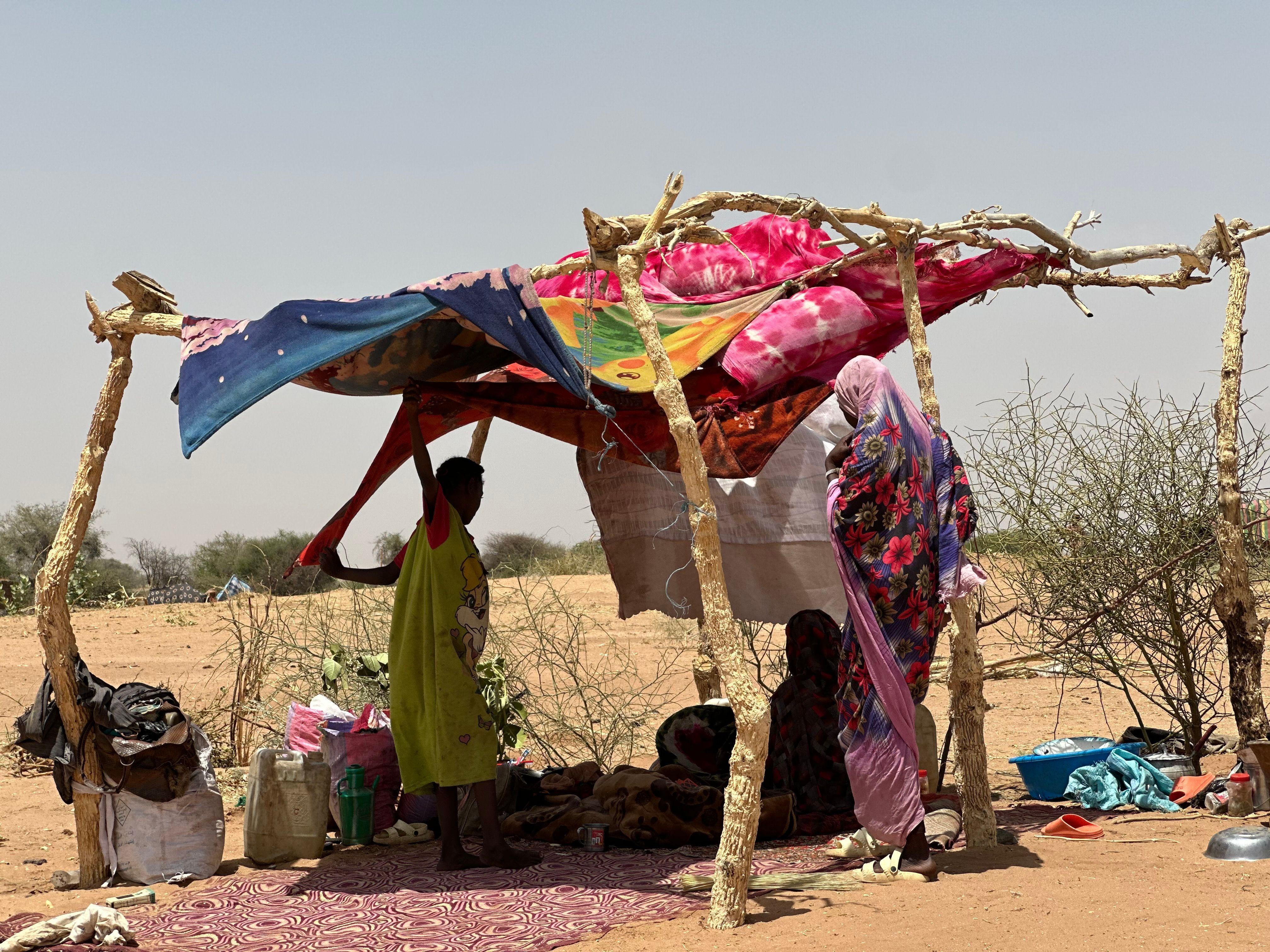 صورة تظهر نازحين سودانيين يحتمون تحت خيمة بدائية الصنع وسط منطقة شبه صحراوية.